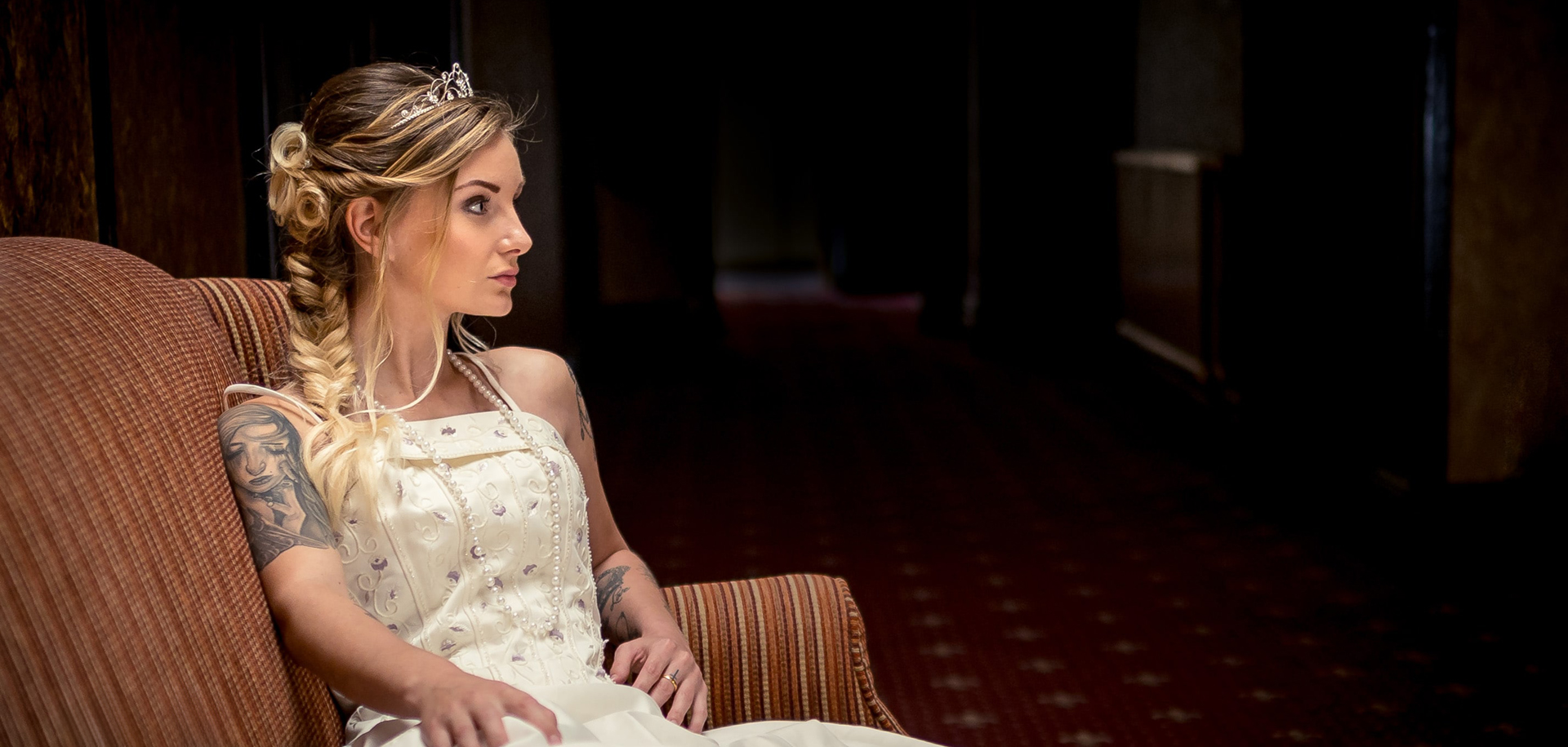 bride sat on a sofa with her dress on and a dark background