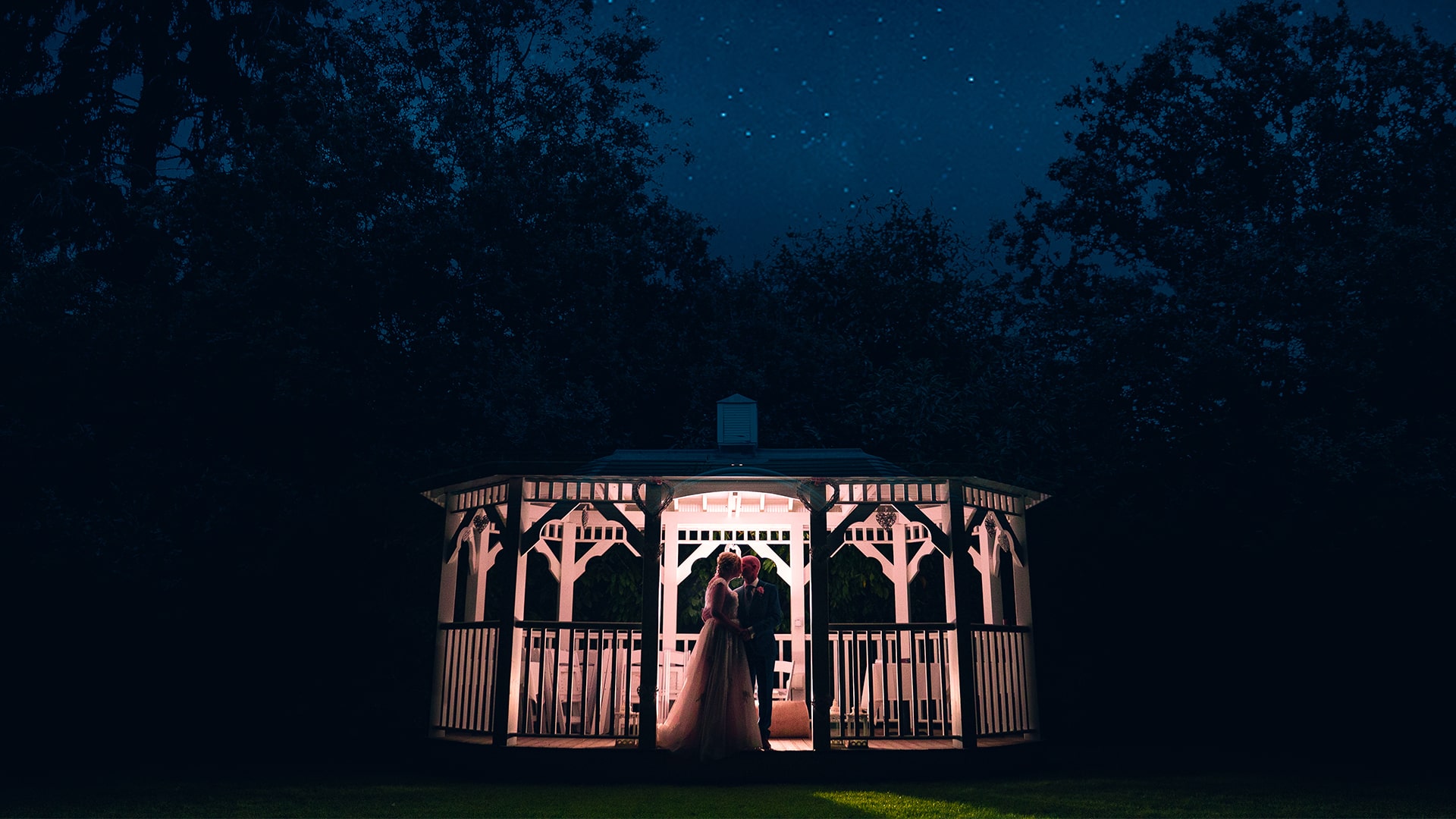 wedding couple on a gazebo at night backlit by flash