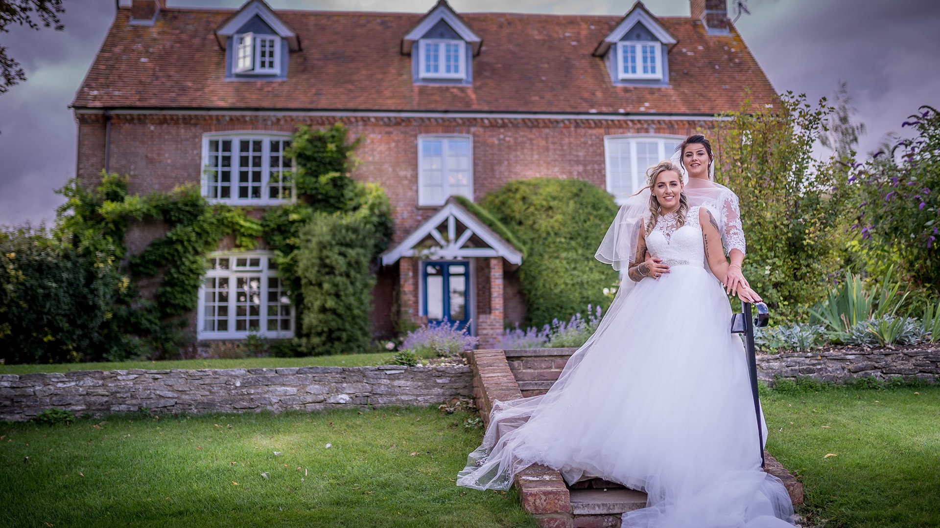 same sex wedding couple stading in front of a house in their wedding dresses