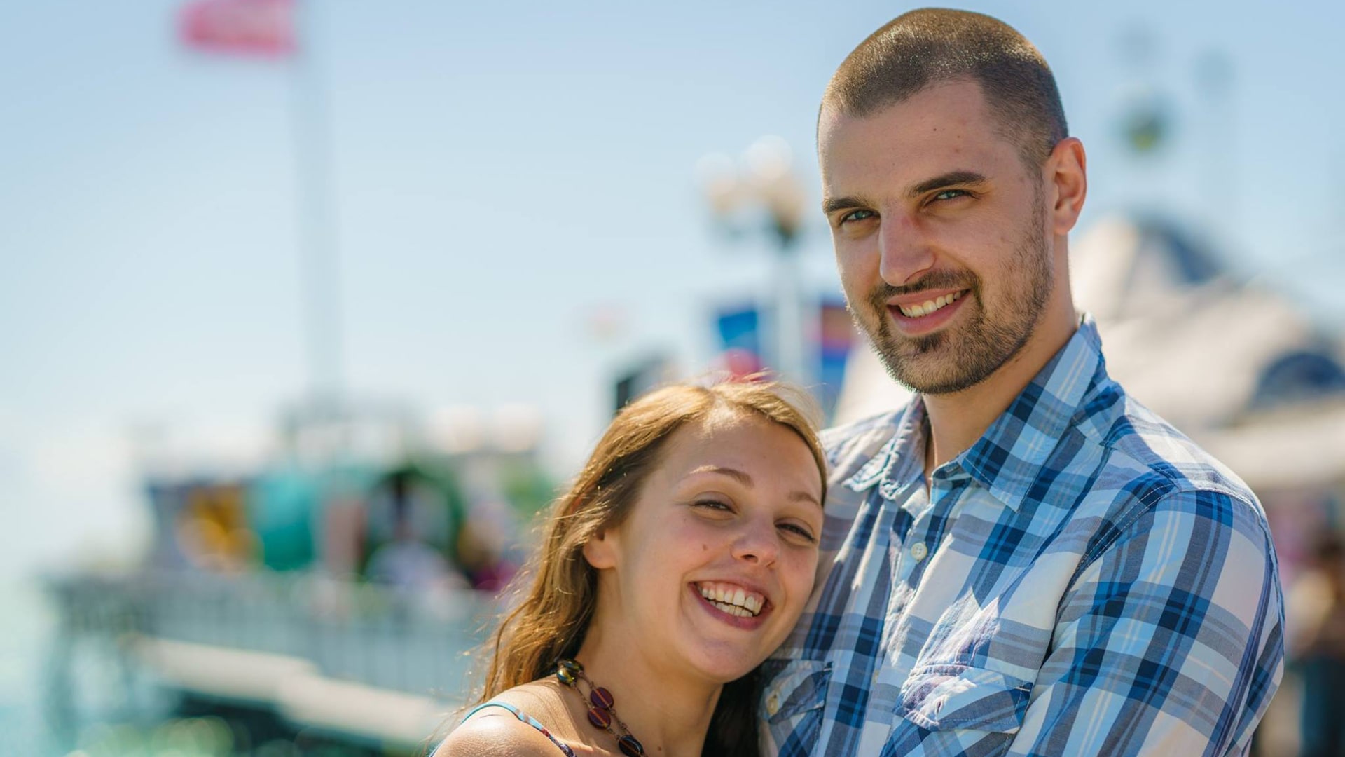 couple posed on brighton pier with the fairground in the background